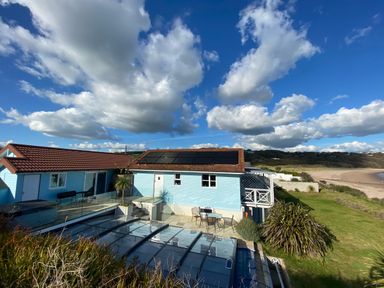 A house with solar panels on the roof a covered pool patio furniture and a beach in the background at The Sandcastle in Freshwater East