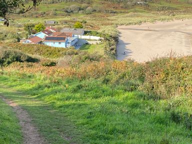 A coastal landscape with a path leading to houses near a sandy beach at The Sandcastle in Freshwater East