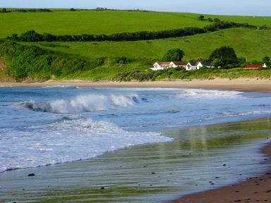 A beach with waves coming ashore and houses near green hills at The Sandcastle in Freshwater East