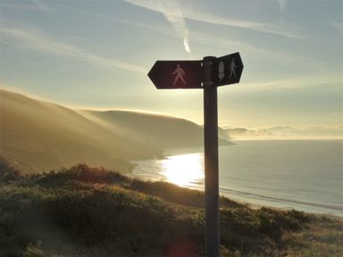 A coastal landscape with a walking path sign and hills at The Sandcastle in Freshwater East