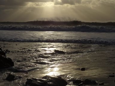 Ocean waves crashing on rocky shore with sun rays breaking through clouds