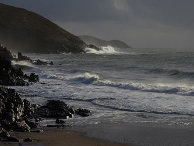 A rocky shoreline with waves breaking on the rocks and hills in the background at The Sandcastle in Freshwater East