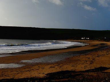 A beach with waves coming ashore and houses in the distance at The Sandcastle in Freshwater East