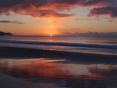 A beach with a sunset over the ocean and reflections on wet sand at The Sandcastle in Freshwater East