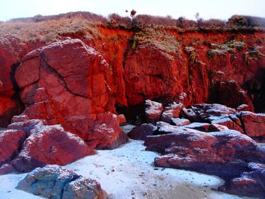 A rocky cliff with red soil and scattered rocks on a sandy beach at The Sandcastle in Freshwater East