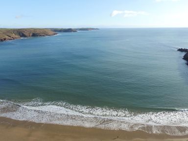 A view of a sandy beach with waves and a rocky coastline in the distance at The Sandcastle in Freshwater East