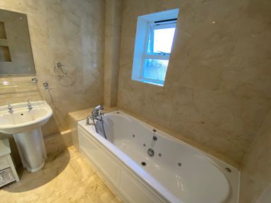 A bathroom with a bathtub a sink a small window and tiled walls at The Sandcastle in Freshwater East
