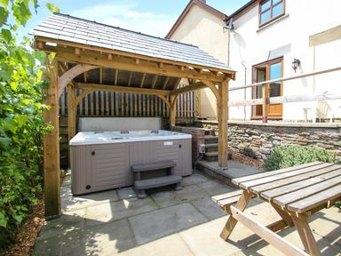 An outdoor area with a hot tub under a wooden pergola and a wooden picnic table at Lilly Cottage in Whitecroft Royal Forest of Dean