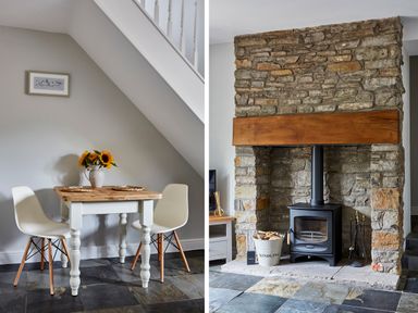 A dining area with a wooden table and two chairs under a staircase and a stone fireplace with a wood burning stove and firewood in a bucket at Lilly Cottage in Whitecroft Royal Forest of Dean