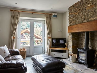 A living room with leather sofa and ottoman a wood burning stove and a television at Lilly Cottage in Whitecroft Royal Forest of Dean