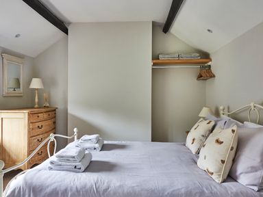 A bedroom with a bed folded towels and pillows a dresser with a lamp and mirror and an open closet with hangers at Lilly Cottage Whitecroft Royal Forest of Dean