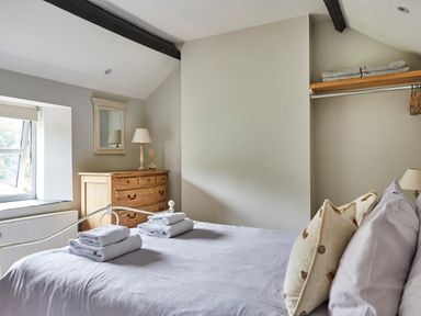 A bedroom with a bed folded towels wooden dresser lamp mirror and window at Lilly Cottage in Whitecroft Royal Forest of Dean