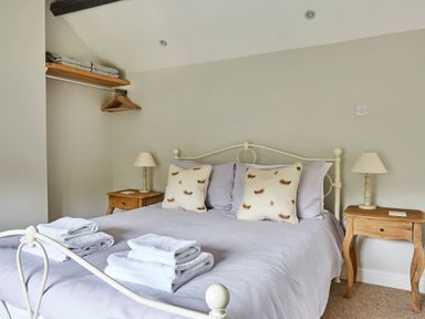 A bedroom with a metal bed frame two bedside tables with lamps and an open wardrobe with hangers and folded towels at Lilly Cottage in Whitecroft Royal Forest of Dean