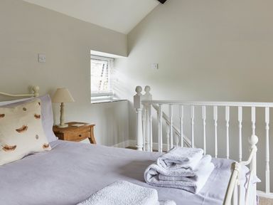 A bedroom with a bed with folded towels a pillow a bedside table with a lamp and a window at Lilly Cottage in Whitecroft Royal Forest of Dean