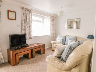 A living room with cream sofas blue cushions a wooden table with a tv and floral curtains at Ducks Ditty in Liskeard