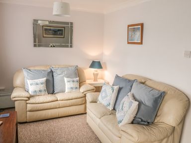 A living room with two beige leather sofas multiple cushions a side table with a lamp a wall mirror and framed pictures at Ducks Ditty in Liskeard