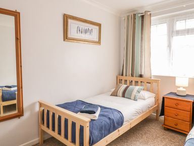 A bedroom with a single wooden bed a bedside table with a lamp a large wall mirror and striped curtains at Ducks Ditty in Liskeard