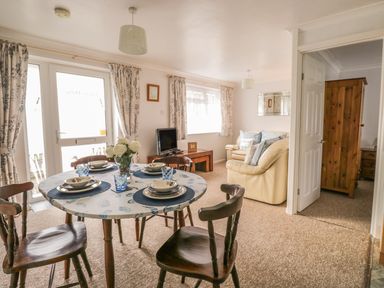 A dining area with a round table set for four and a living room with beige sofas and a TV at Ducks Ditty in Liskeard