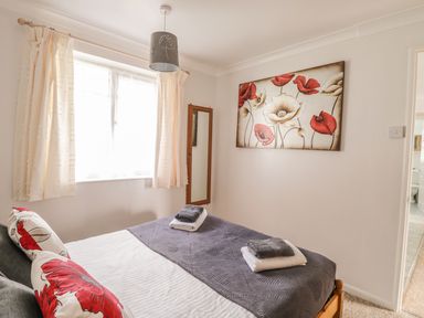 A bedroom with a bed covered with gray blankets and red floral pillows a wall mirror and floral painting at Ducks Ditty in Liskeard