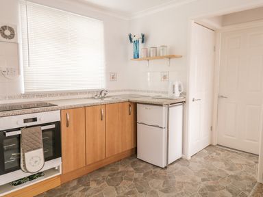 A kitchen with wood cabinets a white oven a small refrigerator a tiled floor and a window with blinds at Ducks Ditty in Liskeard