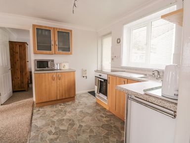A kitchen with wooden cabinets a microwave toaster and kettle on the counters and a sink under a window with blinds at Ducks Ditty in Liskeard