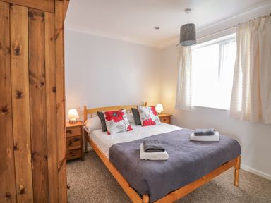 A bedroom with a wooden bed frame bedside tables lamps a wardrobe and a window with curtains at Ducks Ditty in Liskeard