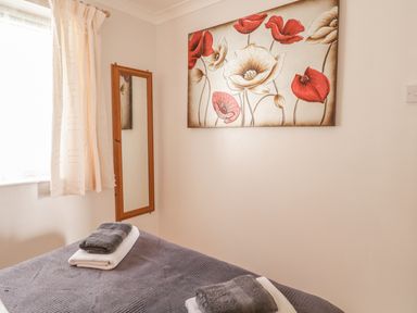 A bedroom with a bed covered in gray linens and towels with a wall mirror and floral painting at Ducks Ditty in Liskeard