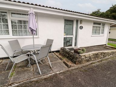 Outdoor patio area with a round table four chairs and a closed umbrella in front of a white building at Ducks Ditty in Liskeard