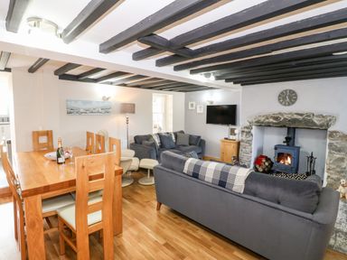 A living room with gray sofas a stone fireplace and a wooden dining table at Min-y-rhos in Edern