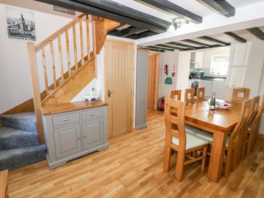 A dining area with wooden table and chairs next to a staircase and kitchen at Min-y-rhos in Edern