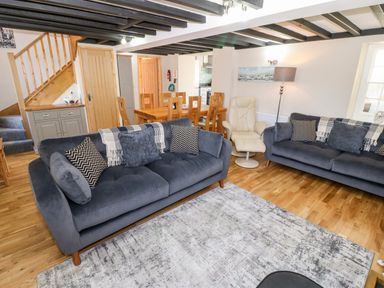 A living room with two blue sofas a wooden dining table and chairs a beige armchair and a staircase at Min-y-rhos in Edern