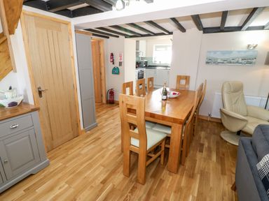 A dining area with a wooden table and chairs next to a kitchen and living space at Min-y-rhos in Edern