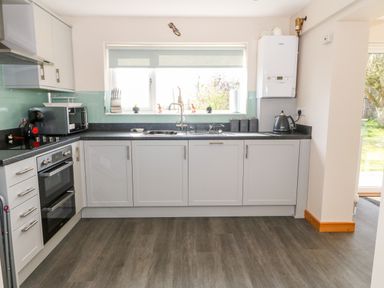 A kitchen with white cabinets black countertop microwave oven kettle and window at Min-y-rhos in Edern