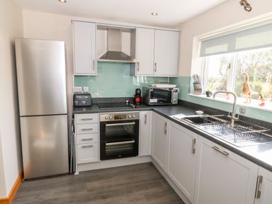 A kitchen with a refrigerator stove microwave toaster sink and window at Min-y-rhos in Edern