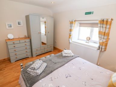 A bedroom with a bed, grey wardrobe, chest of drawers, window with plaid yellow curtains at Min-y-rhos in Edern