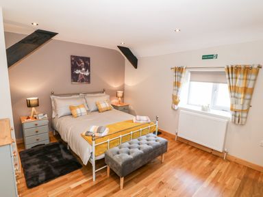 A bedroom with a double bed between two bedside tables with lamps a window with plaid curtains and a cushioned bench at Min-y-rhos in Edern