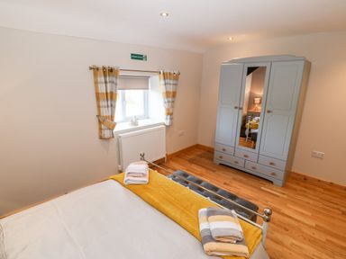 A bedroom with a bed folded towels a gray wardrobe with mirror and a window with curtains at Min-y-rhos in Edern