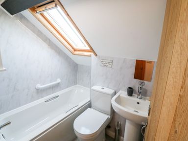 A bathroom with a bathtub under a skylight window a toilet and a pedestal sink at Min-y-rhos in Edern