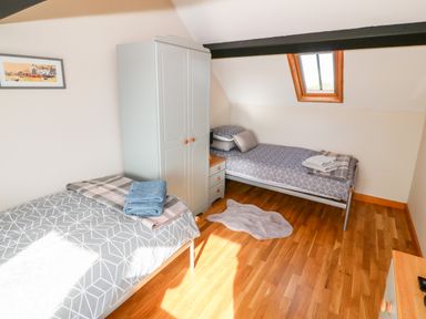 A bedroom with two single beds a wardrobe a nightstand and a small rug on a wooden floor at Min-y-rhos in Edern