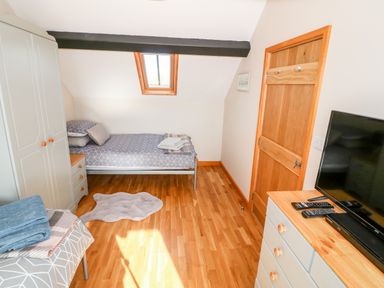 A bedroom with a single bed a wardrobe a chest of drawers a television and a wooden door at Min-y-rhos in Edern