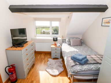 A bedroom with a single bed a nightstand a chest of drawers with a tv and a window showing a green landscape at Min-y-rhos in Edern