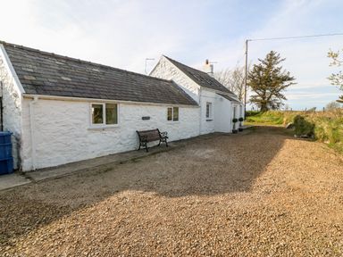 A white stone cottage with a slate roof a bench outside and a gravel driveway at Min-y-rhos in Edern