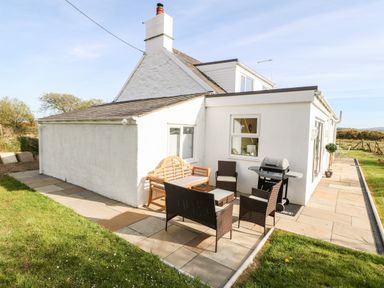 An outdoor patio with table chairs barbecue and a wooden bench beside a white house at Min-y-rhos in Edern
