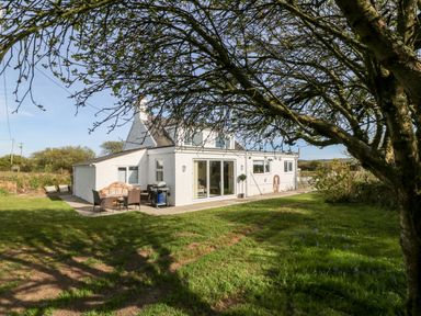 A white house with a patio and outdoor furniture in a garden with trees at Min-y-rhos in Edern