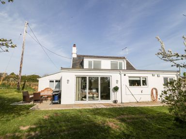 A white house with a patio and outdoor furniture in a grassy yard at Min-y-rhos in Edern