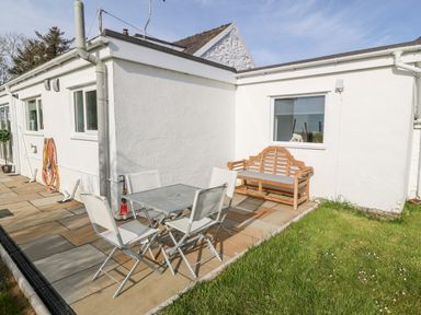 An outdoor patio with a metal table and four chairs and a wooden bench near a white building at Min-y-rhos in Edern