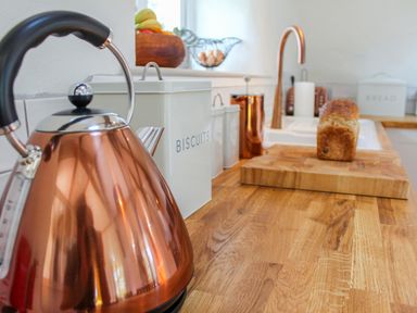 A kitchen counter with a copper kettle biscuits container a cutting board with a loaf of bread and a sink at Sunbury Barn in St Agnes