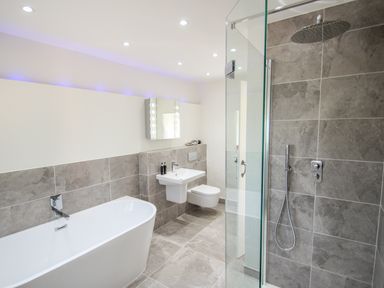 A bathroom with a bathtub a sink a toilet and a shower with gray tiled walls at Sunbury Barn in St Agnes