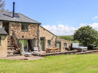 An outdoor patio with lounge chairs a picnic table a barbecue hot tub and grassy lawn at Sunbury Barn in St Agnes