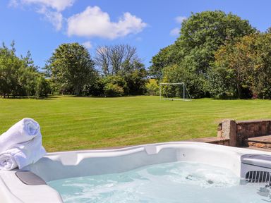 An outdoor hot tub with white towels beside a large grass field with a soccer goal and trees at Sunbury Barn in St Agnes